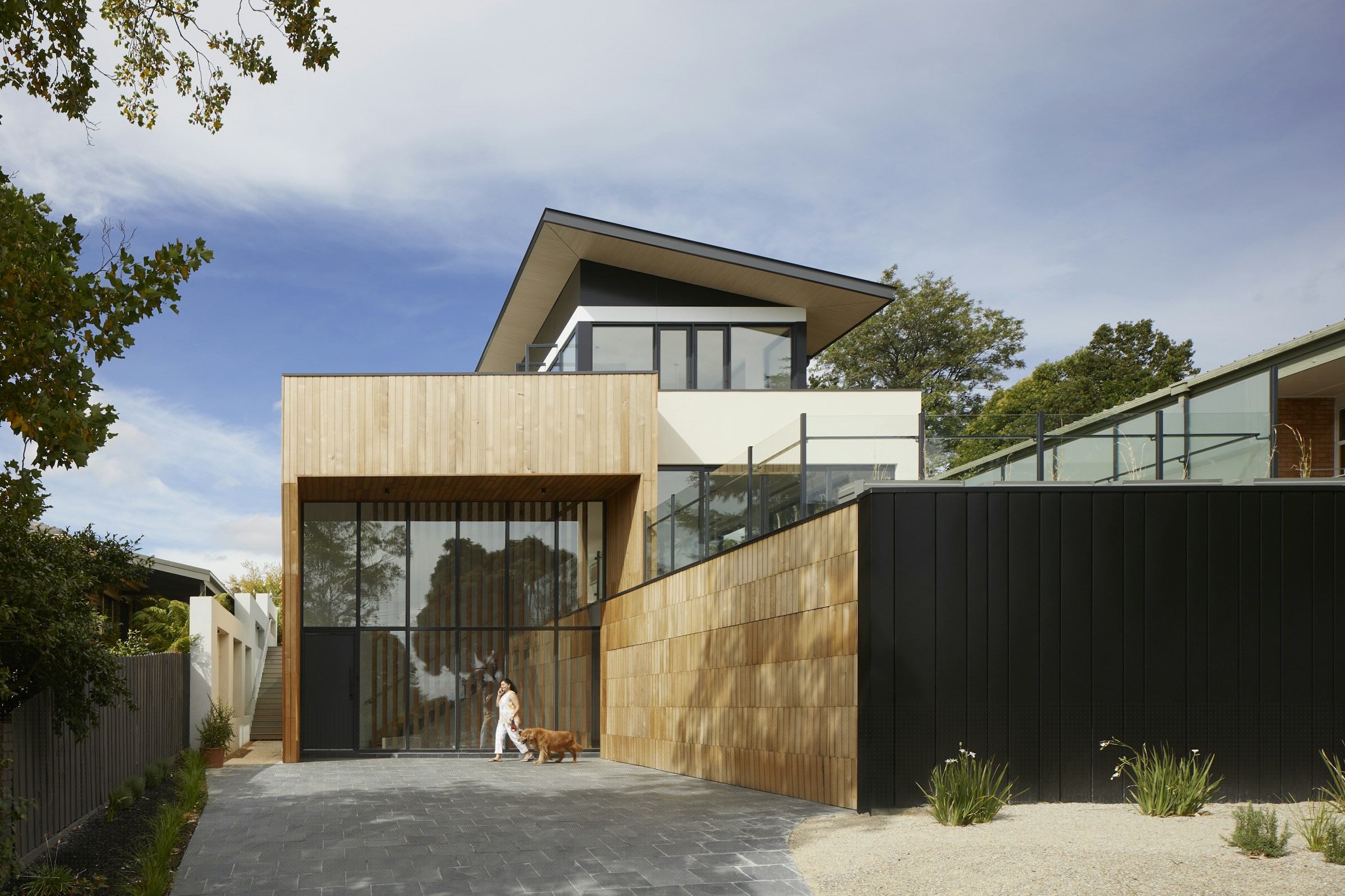 Timber-clad house with a raked roof and a dark fence beside a gravel drive